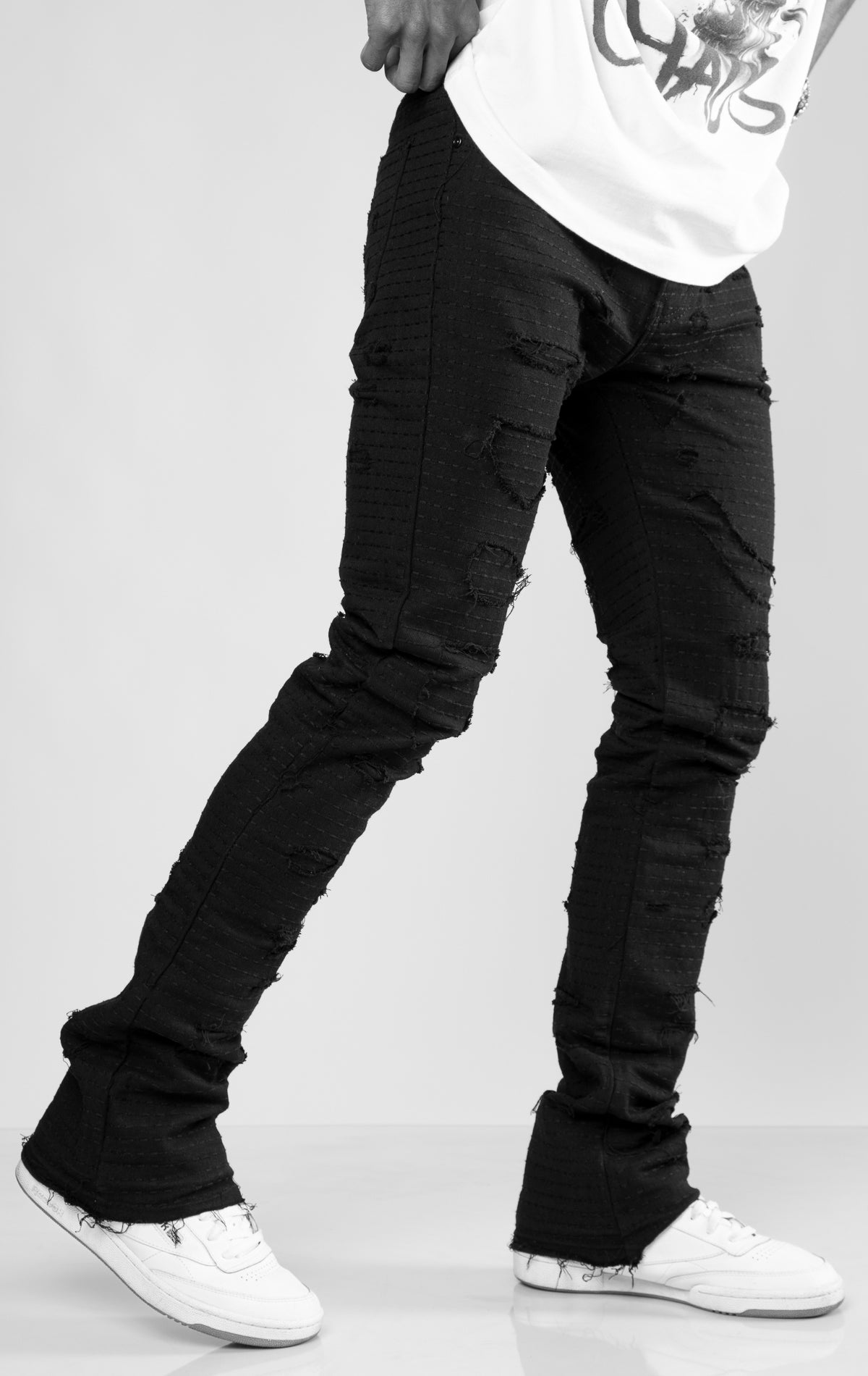 Jet black distressed denim jeans with ripped details and a stacked fit at the ankle.