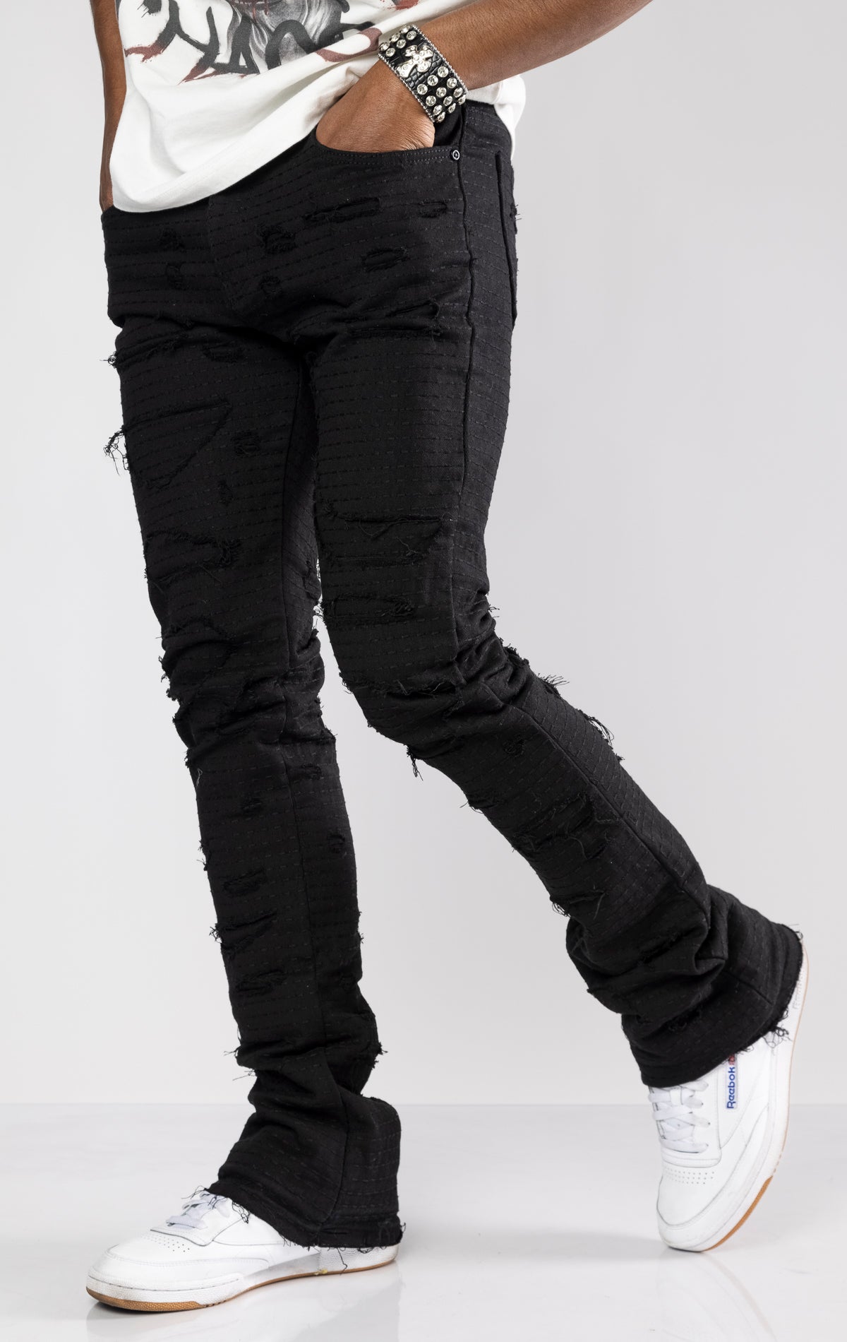 Jet black distressed denim jeans with ripped details and a stacked fit at the ankle.