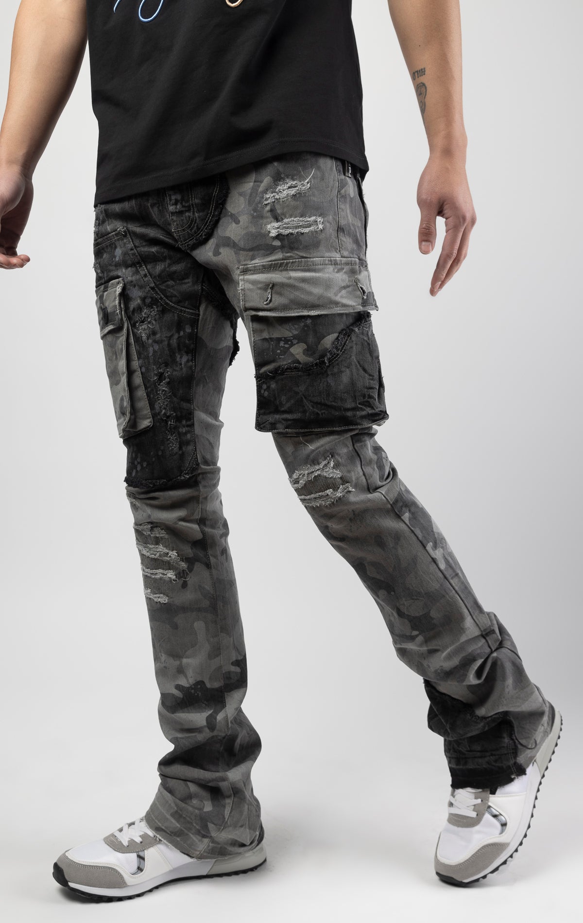 Black camo Extended length flare pant with a regular rise for maximum stacks. Skinny fit with hand-smearing and speckled paint splatter throughout. Rip and repair detailing, accompanied by cut & sewn woodland camouflage twill patches. Stitching repairs and deep front pocket bags, perfect for large smart phones.