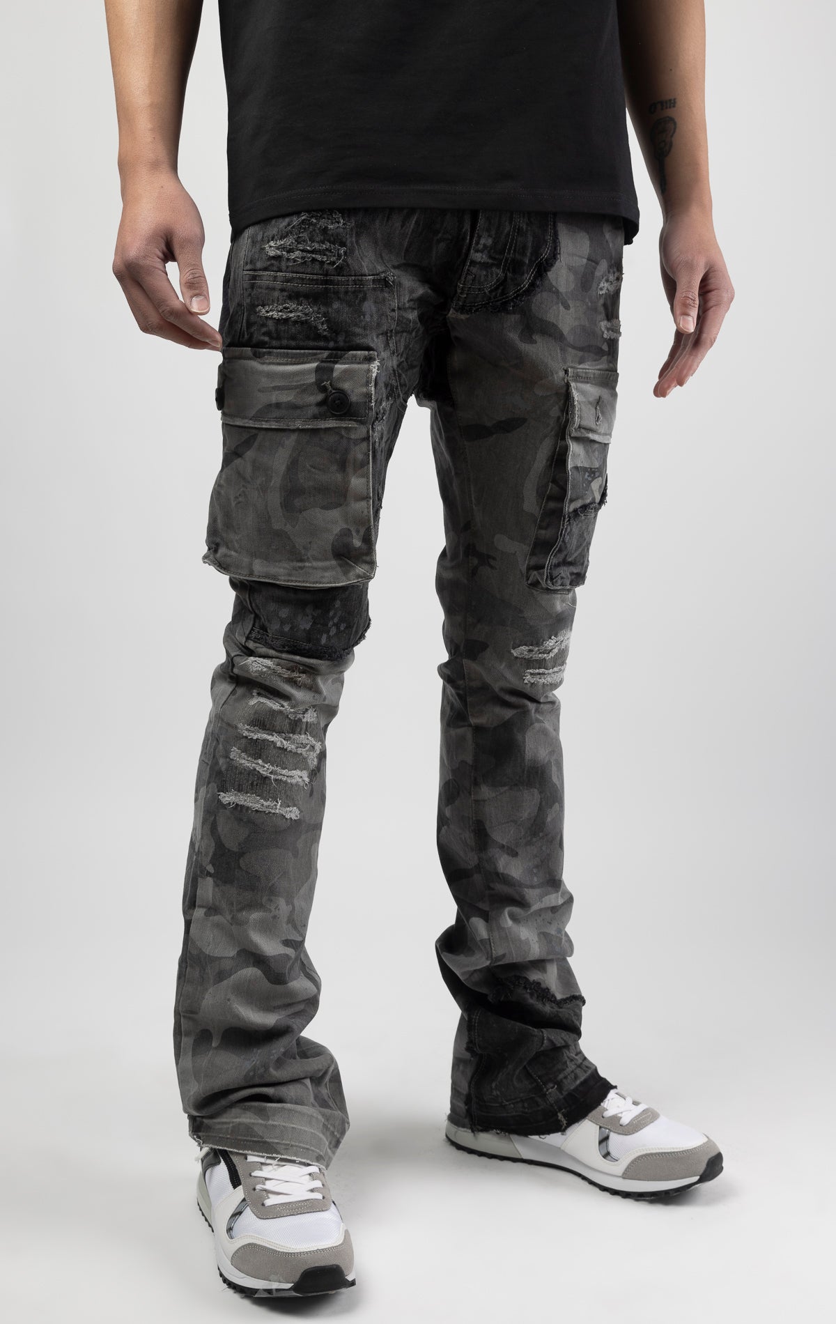 Black camo Extended length flare pant with a regular rise for maximum stacks. Skinny fit with hand-smearing and speckled paint splatter throughout. Rip and repair detailing, accompanied by cut & sewn woodland camouflage twill patches. Stitching repairs and deep front pocket bags, perfect for large smart phones.
