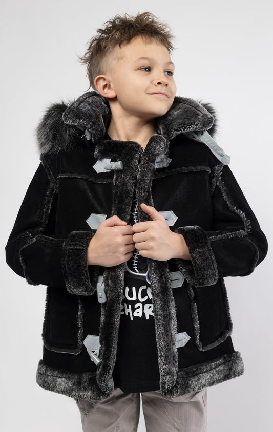 Black jacket lined with plush faux shearling throughout the body and sleeves. It also features shearling-accented pockets, a horn toggle front closure, and vegan suede straps with a buckle at the neck. For added convenience, a detachable faux fox fur hood with a zipper is included. This product is also available for adults.