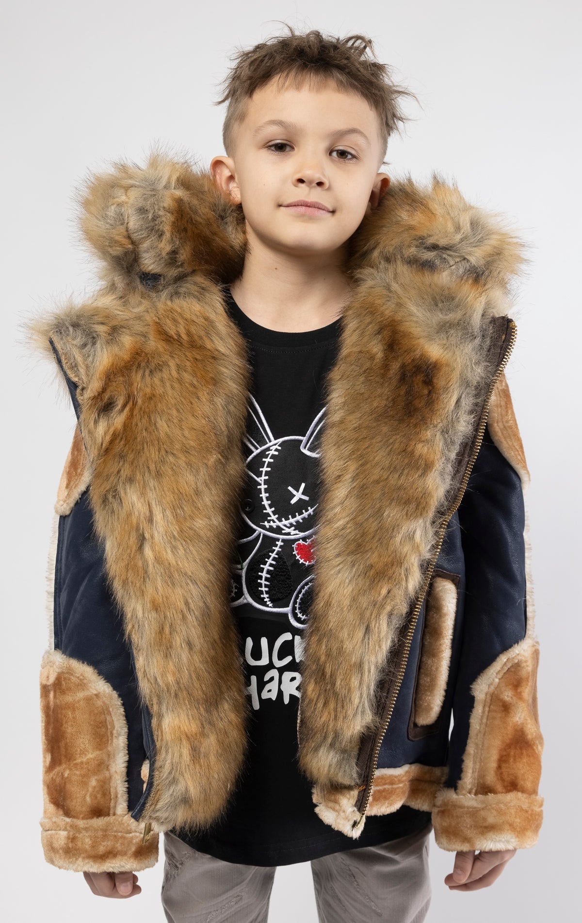 Faux suede body. Soft faux shearling lining on the body, sleeves, and pockets. Toggle front closure with vegan suede straps and a buckle at the neck. Detachable hood made of faux fox fur with a zipper.