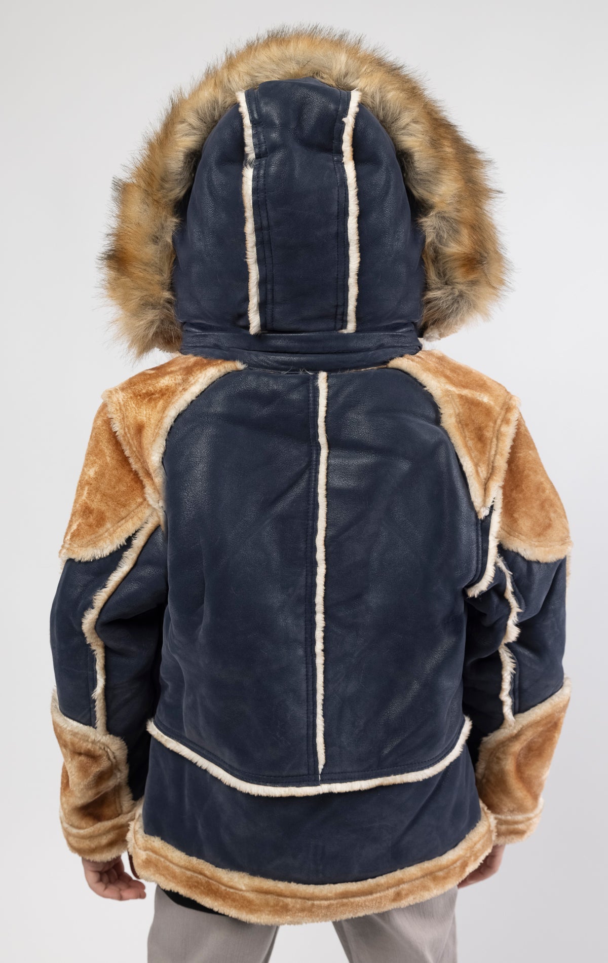 Faux suede body. Soft faux shearling lining on the body, sleeves, and pockets. Toggle front closure with vegan suede straps and a buckle at the neck. Detachable hood made of faux fox fur with a zipper.