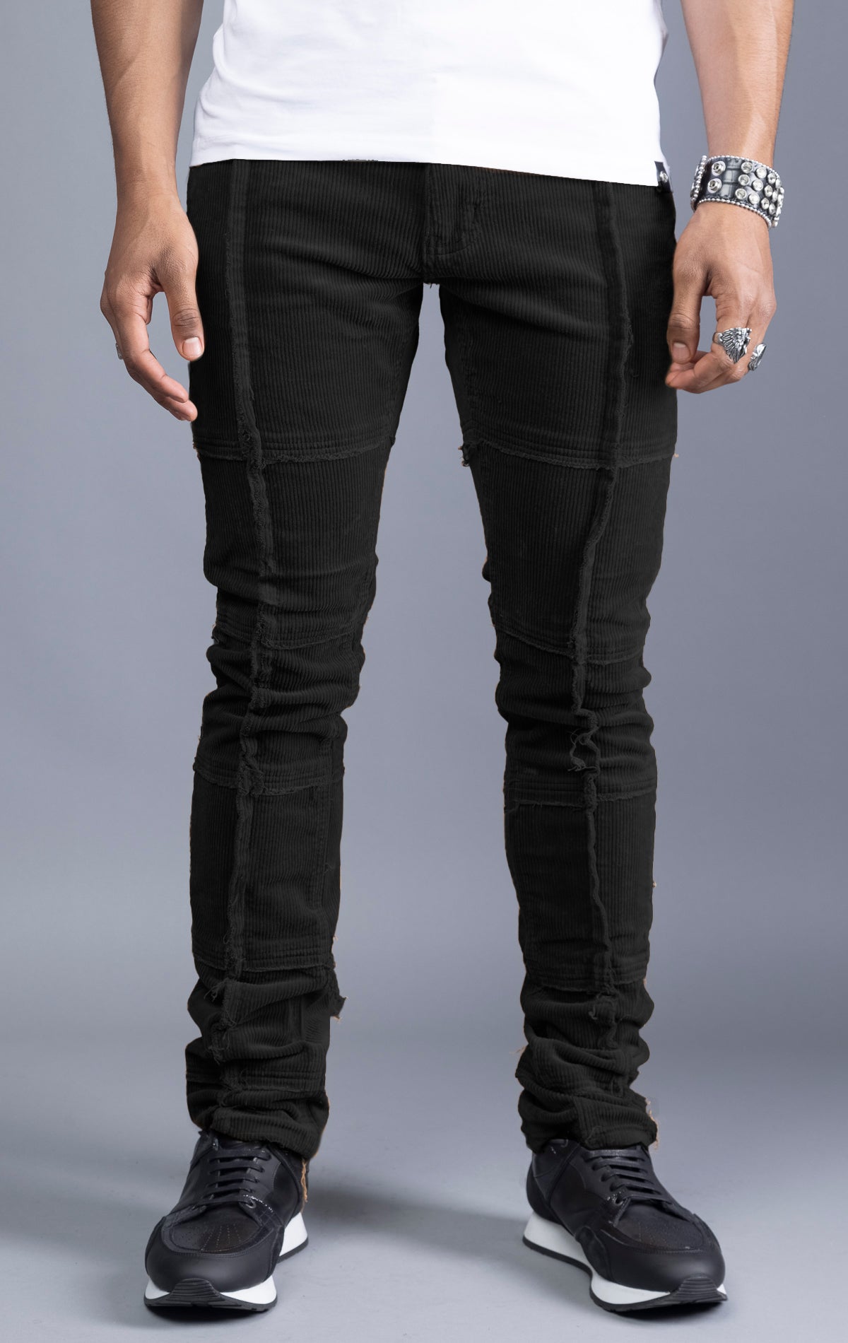 Men's black corduroy pants with stacked legs, cut-and-sew details, and raw hems.
