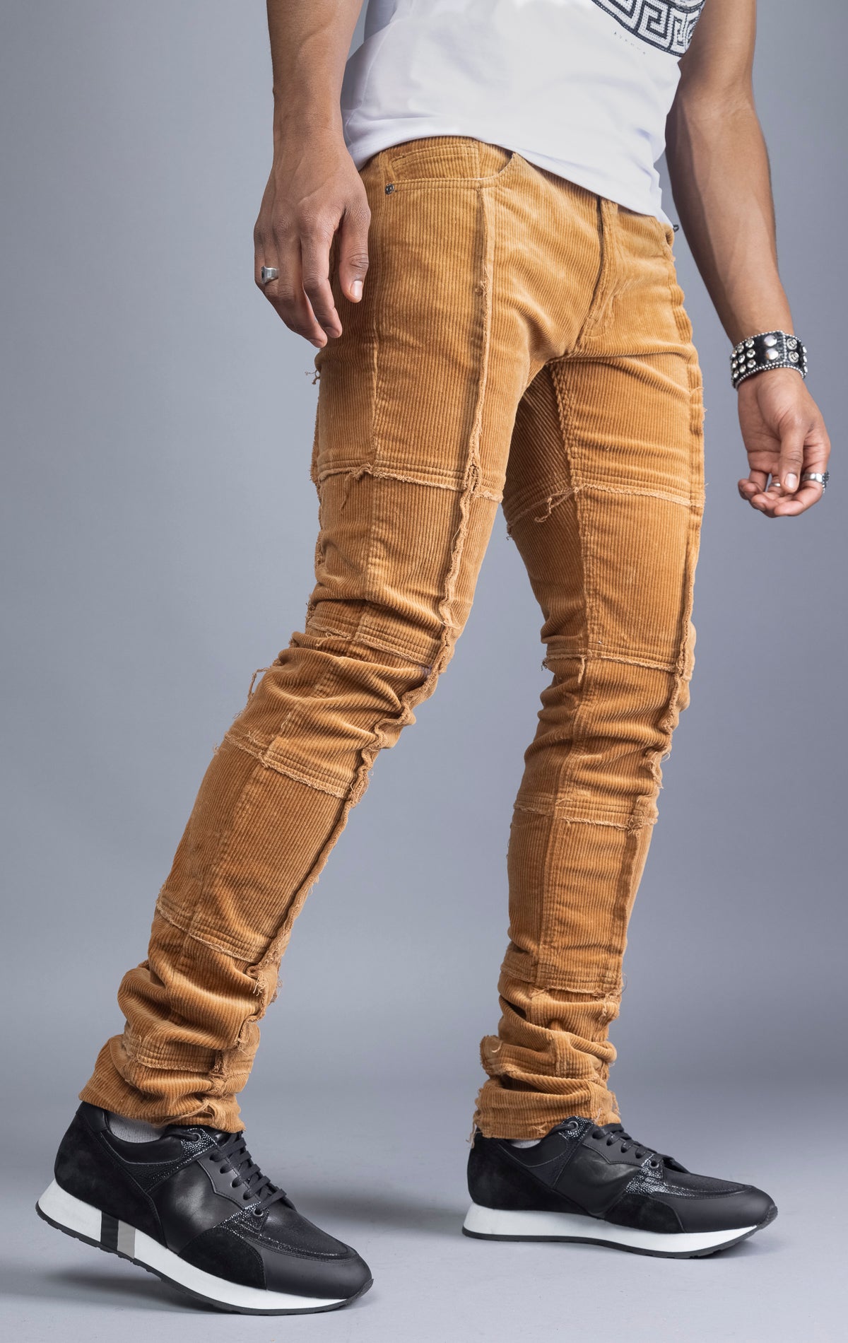 Men's camel corduroy pants with stacked legs, cut-and-sew details, and raw hems.