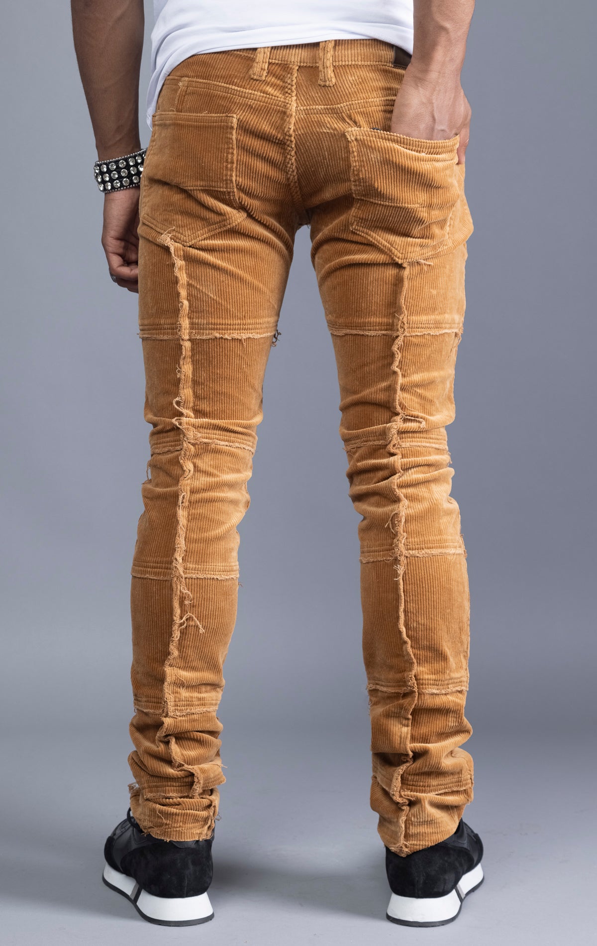 Men's camel corduroy pants with stacked legs, cut-and-sew details, and raw hems.