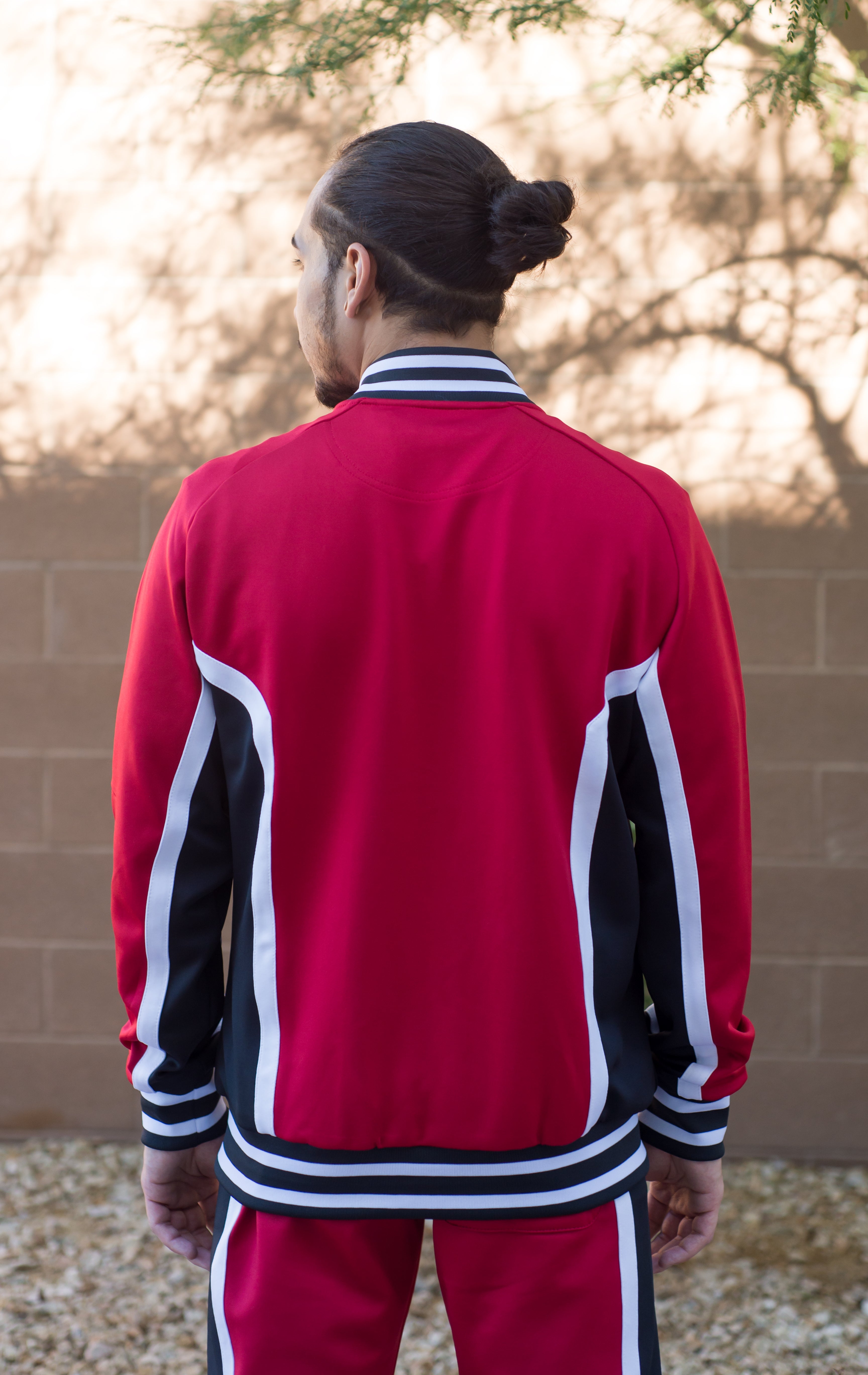 Red track suit back. Track suit top: Full zip track top silhouette with metal zipper. Dual pockets at sides. Cut & sewn contrast stripe detailing. Yarn dyed contrast stripe ribbing. 100% Polyester jersey bound mesh inside lining. Extremely smooth material and soft to the touch. Track suit bottom: Tapered-leg track pant silhouette, rubber dipped drawstrings with metal tips. Dual pockets at sides and zipper gussets at both inner ankle openings.