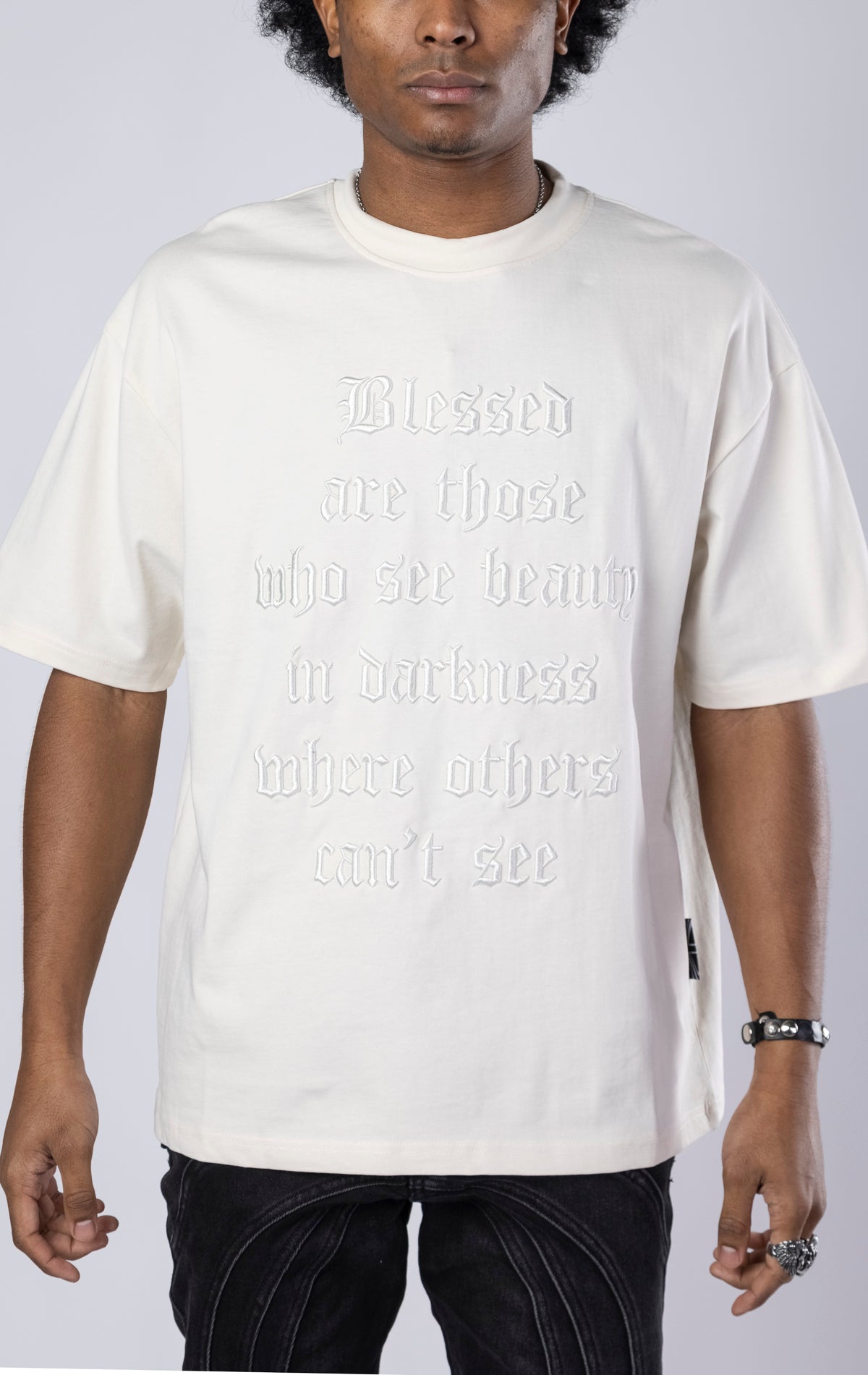 Blessed Darkness Boxy Tee. Cream t-shirt made from 100%  250gr cotton. Features a boxy fit, dropped shoulders, longer sleeves, a 3D embroidered front message, and subtle "blessed" branding