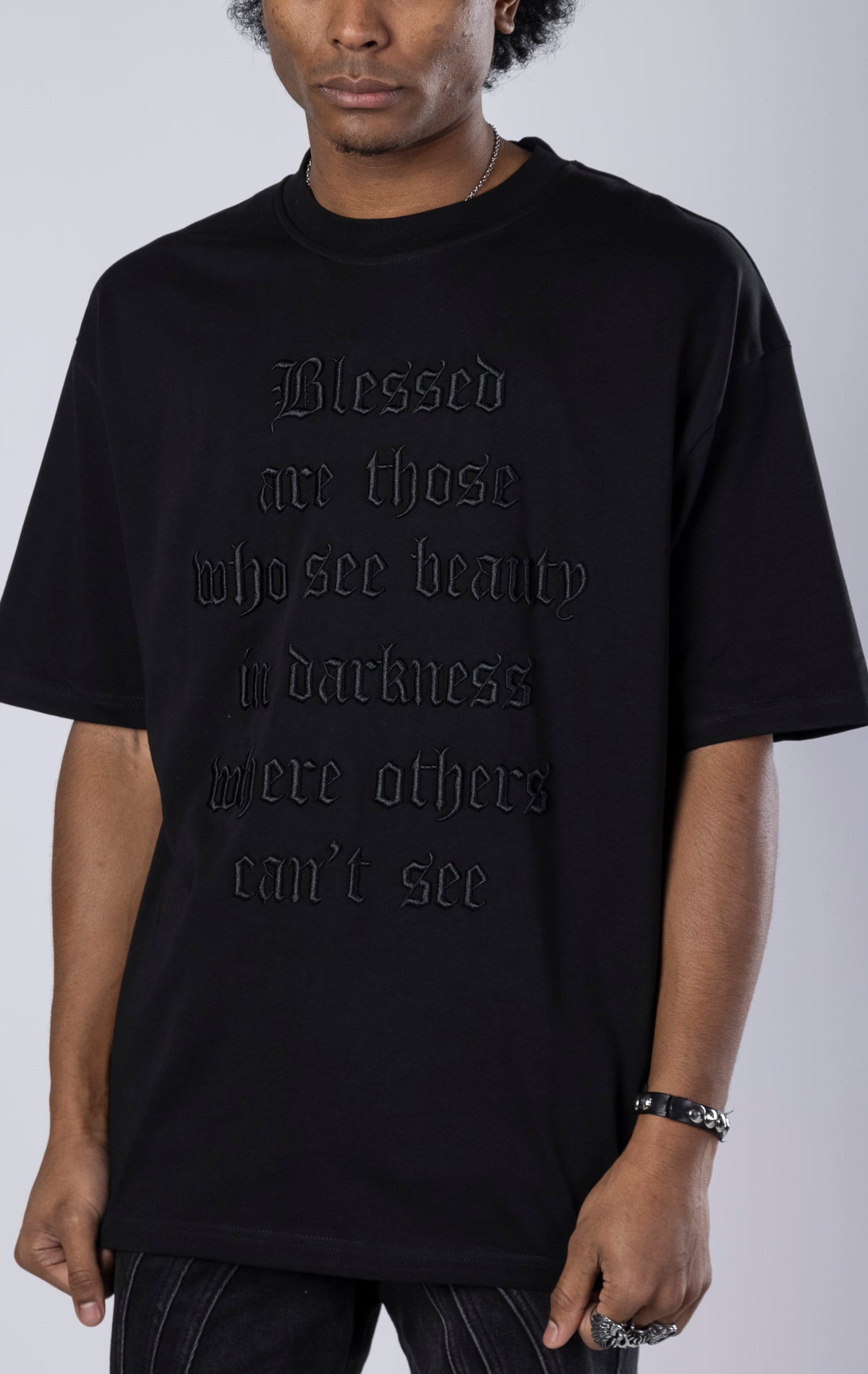 Blessed Darkness Boxy Tee. Black t-shirt made from 100% heavy black 250gr cotton. Features a boxy fit, dropped shoulders, longer sleeves, a 3D embroidered front message, and subtle "blessed" branding