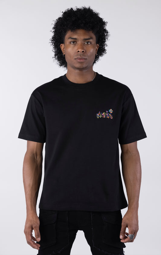 Black short-sleeve t-shirt showing the back, featuring a large, colorful, graffiti-style illustration of a cartoon character in a backwards cap and crown. The text "Bubu" and other tags surround the central image.