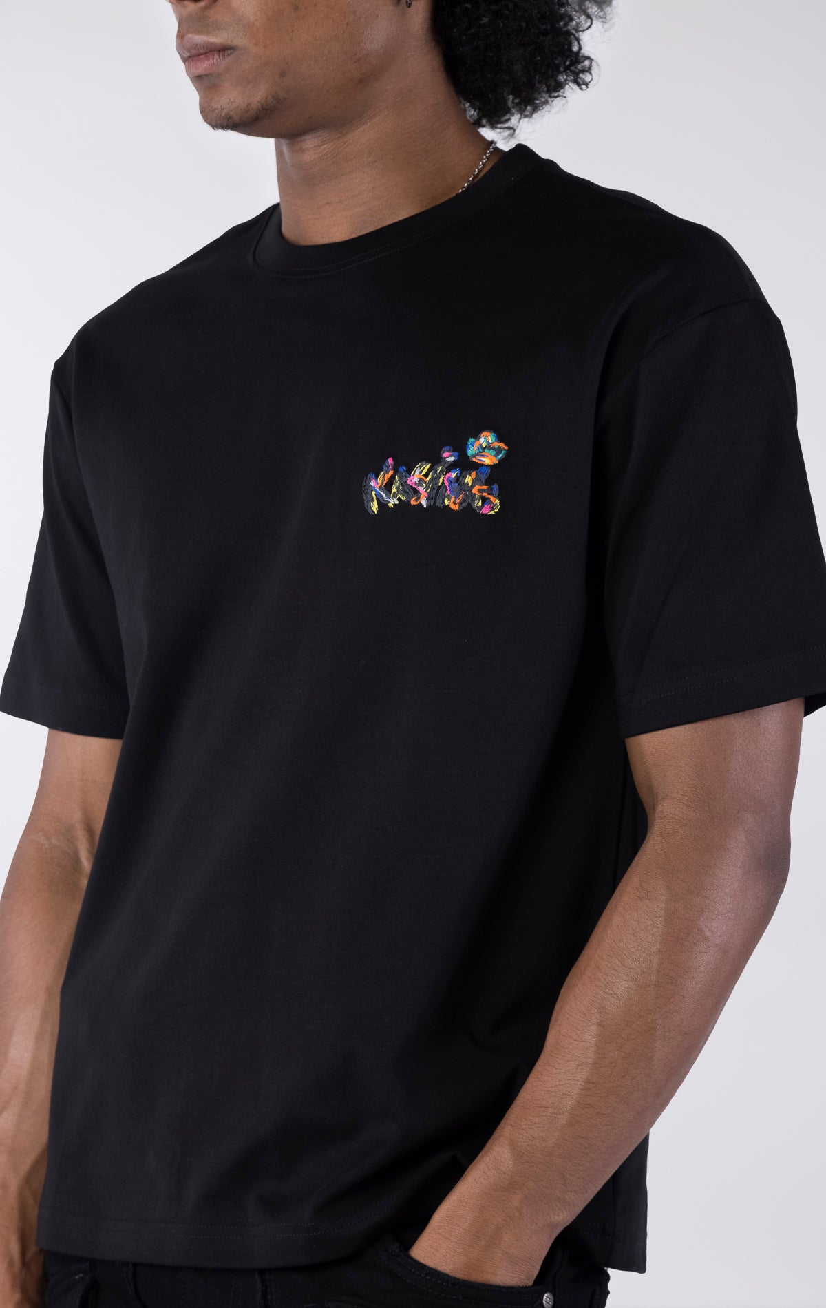 Black short-sleeve t-shirt showing the back, featuring a large, colorful, graffiti-style illustration of a cartoon character in a backwards cap and crown. The text 