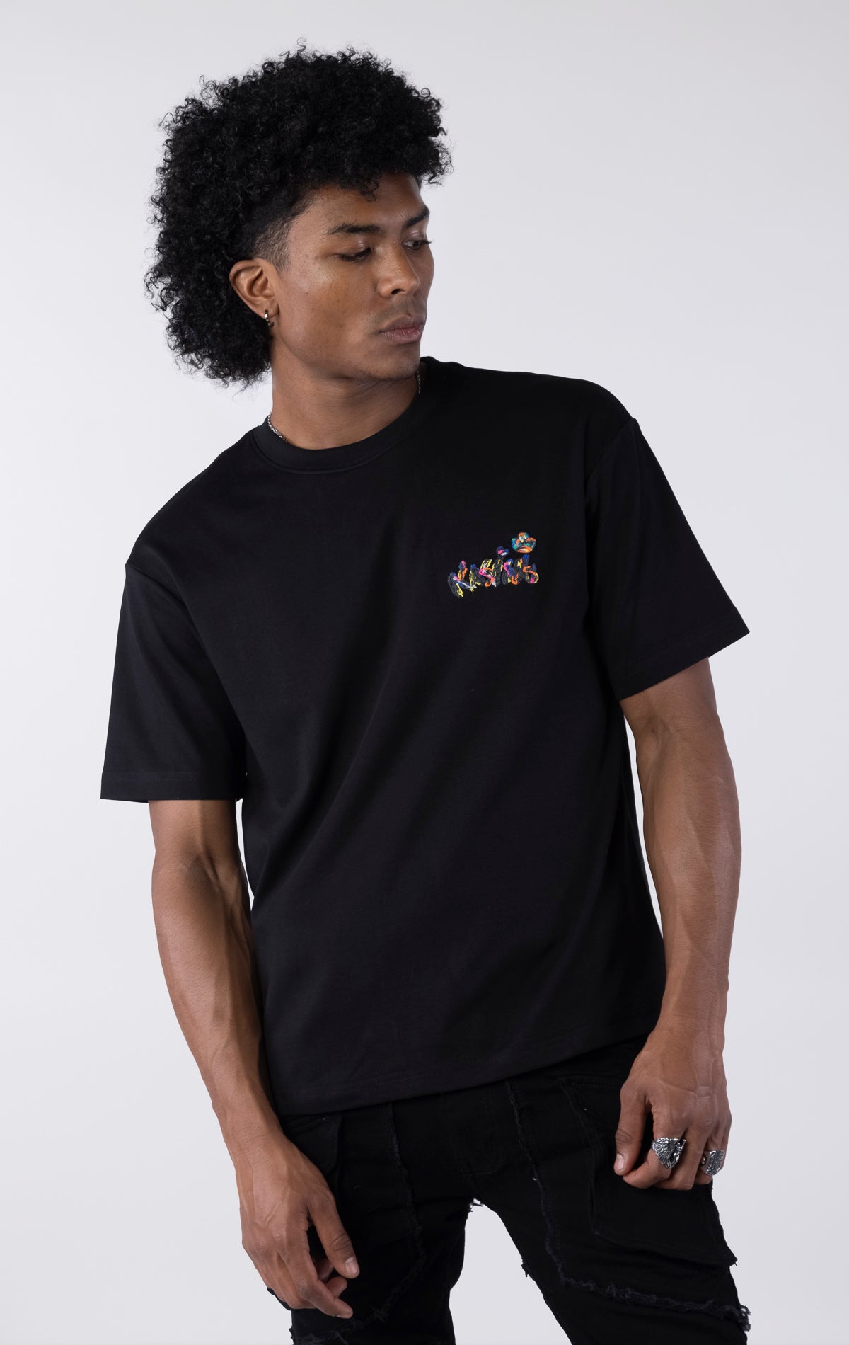 Black short-sleeve t-shirt showing the back, featuring a large, colorful, graffiti-style illustration of a cartoon character in a backwards cap and crown. The text 
