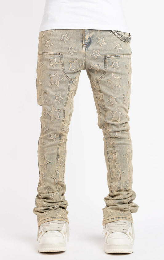 Light vintage wash denim jeans with an all-over embroidered star pattern. The jeans have a slim fit and are stacked at the ankles over white sneakers, featuring a silver chain accent on the front pocket.