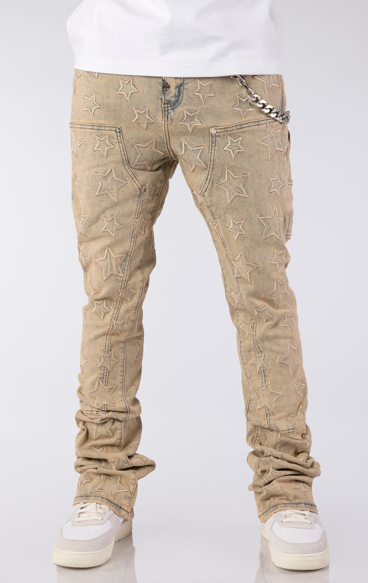 Light vintage wash denim jeans with an all-over embroidered star pattern. The jeans have a slim fit and are stacked at the ankles over white sneakers, featuring a silver chain accent on the front pocket.