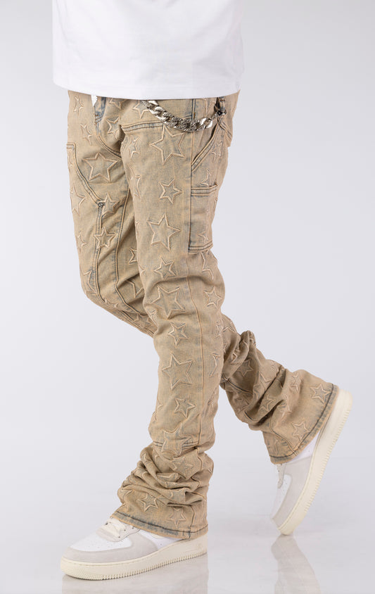 Light vintage wash denim jeans with an all-over embroidered star pattern. The jeans have a slim fit and are stacked at the ankles over white sneakers, featuring a silver chain accent on the front pocket.