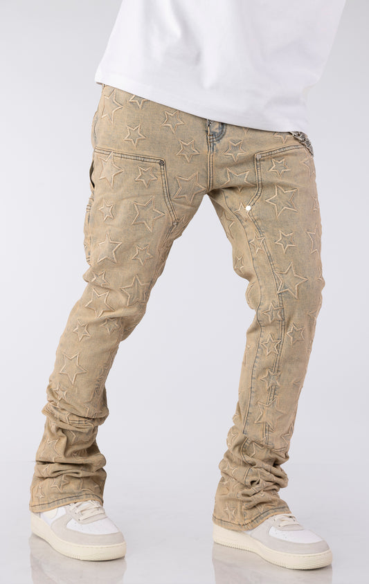 Light vintage wash denim jeans with an all-over embroidered star pattern. The jeans have a slim fit and are stacked at the ankles over white sneakers, featuring a silver chain accent on the front pocket.
