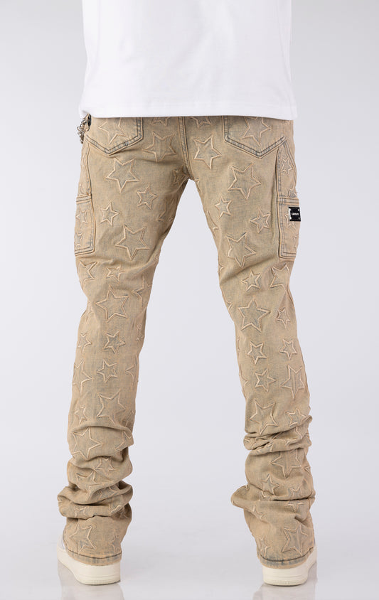 Light vintage wash denim jeans with an all-over embroidered star pattern. The jeans have a slim fit and are stacked at the ankles over white sneakers, featuring a silver chain accent on the front pocket.