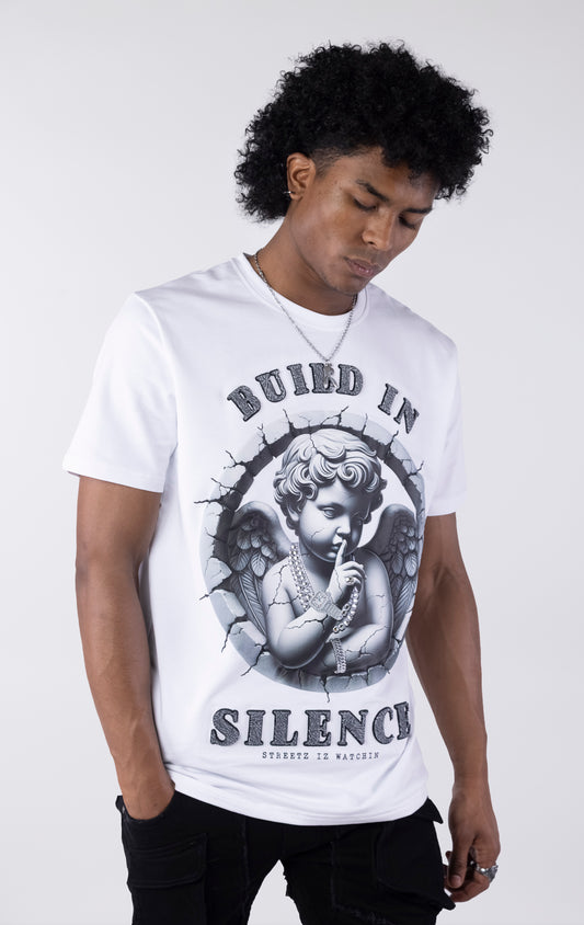 White t-shirt with a large graphic of a monochromatic cherub statue wearing chains and holding a finger to its lips. The graphic is surrounded by cracked stone and the text "BUILD IN SILENCE" is printed above and below in a textured black font.
