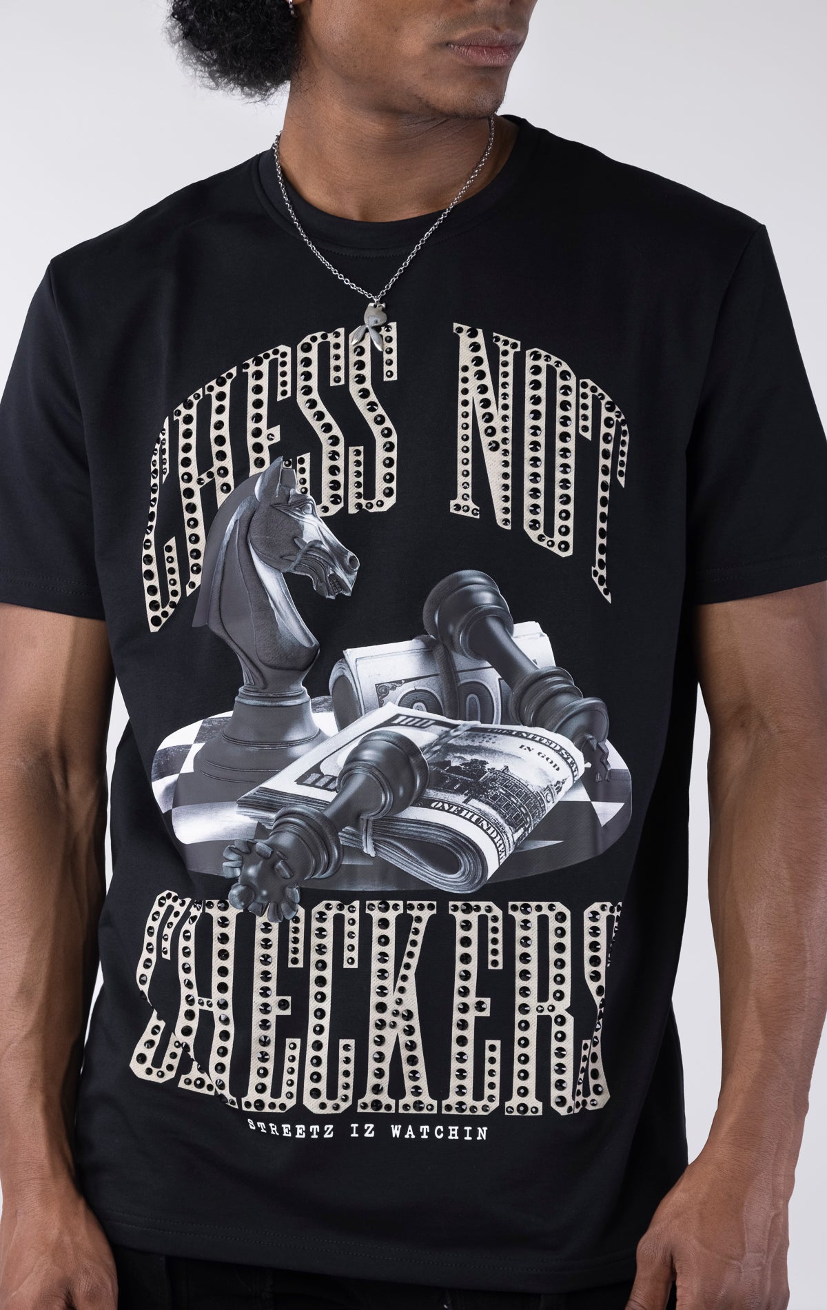 Black t-shirt with a large graphic featuring a black chess knight, fallen pawns, and stacks of money on a checkered surface. The text "CHESS NOT" and "CHECKERS" is printed above and below the graphic in a sparkling white-outlined font.