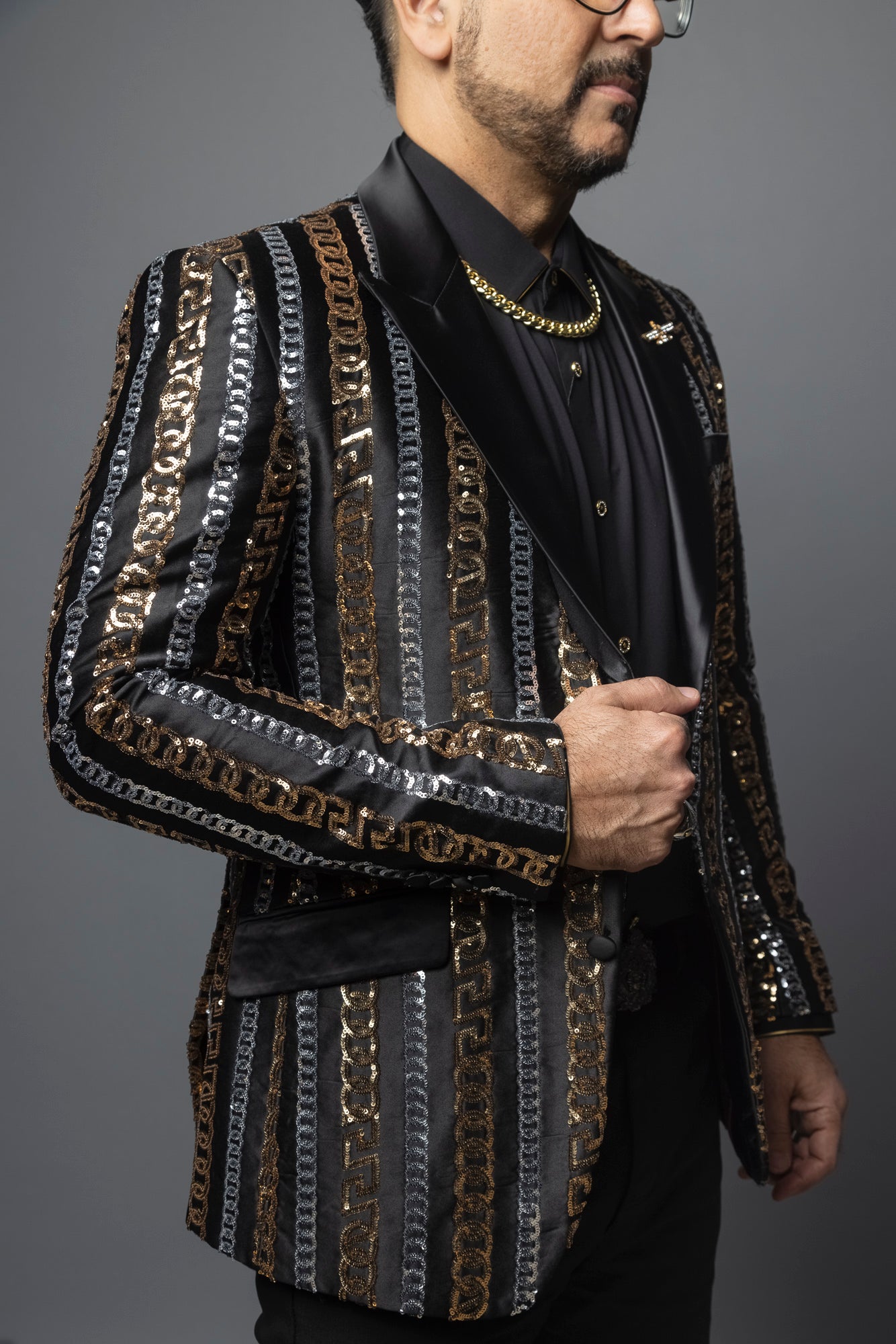 Men's slim-fit blazer with a satin notch lapel, long sleeves, and two-button closure. The blazer features a unique pattern combining Cuban chain, Greek key, and sequin designs. Made from 100% regenerated fiber.