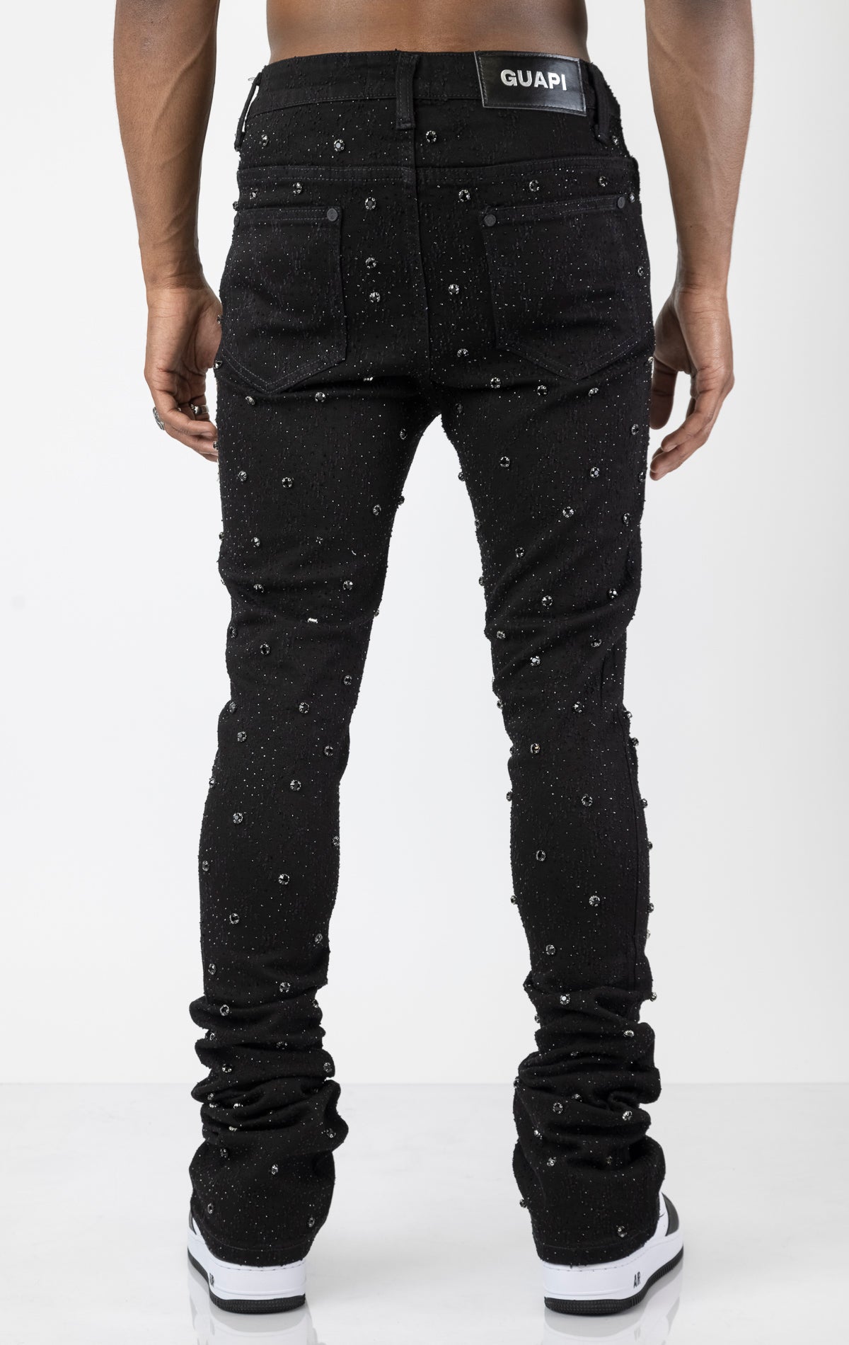 Men's black, tapered-fit jeans with a luxurious cotton-blend fabric (98% cotton, 2% elastane) and custom hardware. The jeans feature subtle laser distressing throughout, delicate diamond embellishments, and a five-pocket design. They stack comfortably above the ankle.