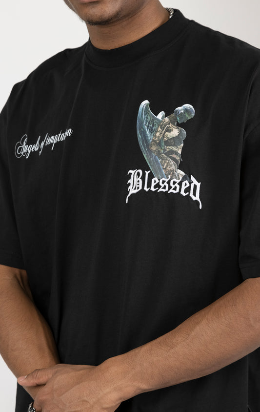Men's boxy fit t-shirt in black. The shirt features dropped shoulders, longer sleeves, and a wide, fitted neck rib. It has "Angels of Temptation" printed on the front and back with 3D "blessed" embroidery on the chest and back. Made from 100% cotton jersey (190gsm). A "blessed" slogan is printed on the inner neck binding.