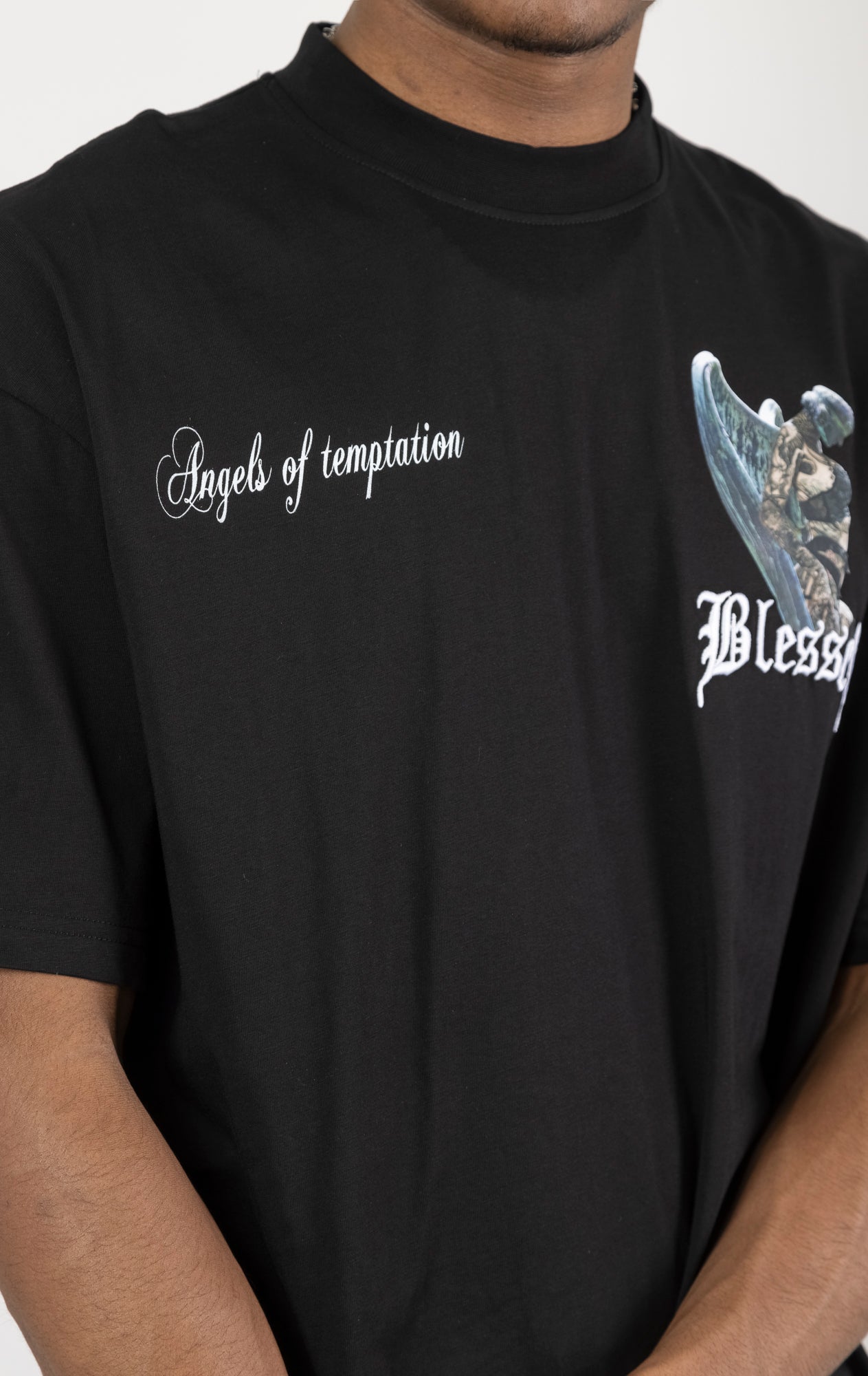 Men's boxy fit t-shirt in black. The shirt features dropped shoulders, longer sleeves, and a wide, fitted neck rib. It has "Angels of Temptation" printed on the front and back with 3D "blessed" embroidery on the chest and back. Made from 100% cotton jersey (190gsm). A "blessed" slogan is printed on the inner neck binding.