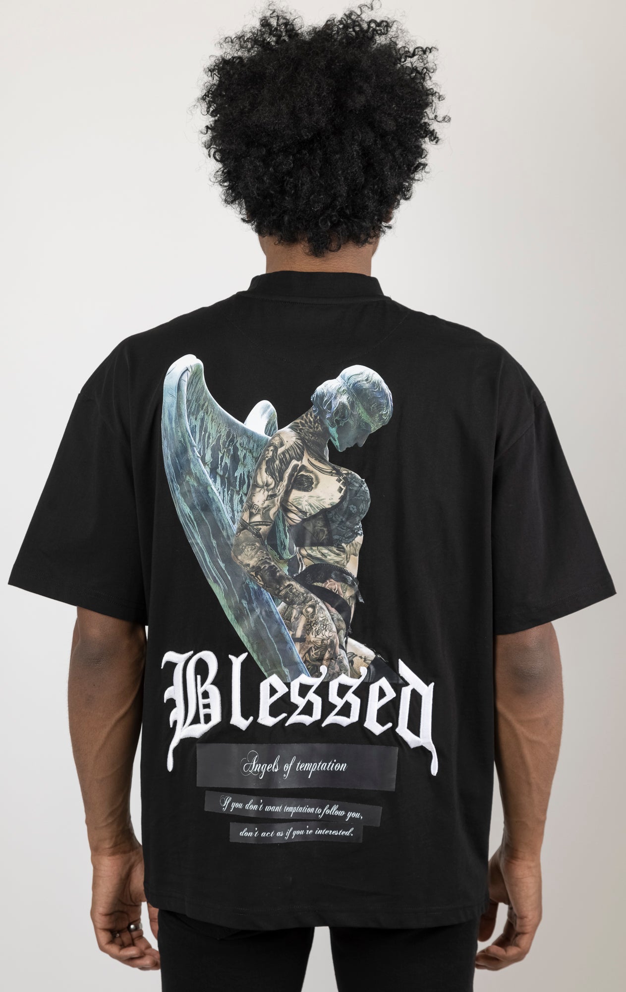 Men's boxy fit t-shirt in black. The shirt features dropped shoulders, longer sleeves, and a wide, fitted neck rib. It has "Angels of Temptation" printed on the front and back with 3D "blessed" embroidery on the chest and back. Made from 100% cotton jersey (190gsm). A "blessed" slogan is printed on the inner neck binding.