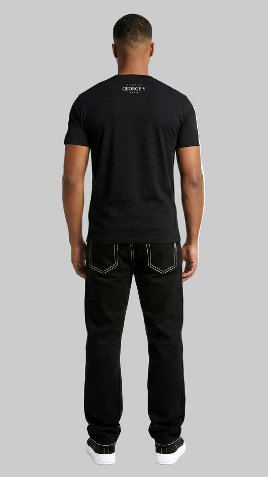 A man viewed from behind wearing a black short-sleeve t-shirt with a small white logo on the upper back, paired with black jeans and white sneakers, against a plain white studio background.