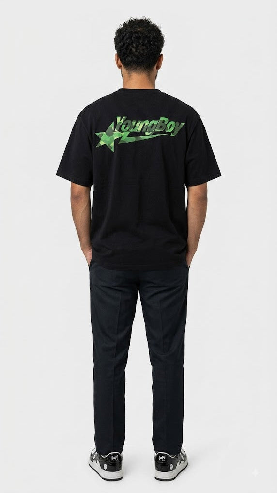 A man viewed from behind wearing a black t-shirt with a green 'YoungBoy' logo on the back, paired with black pants and sneakers, against a light gray studio background.