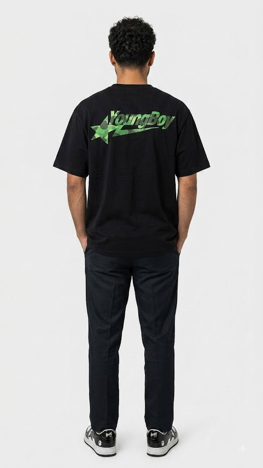 A man viewed from behind wearing a black t-shirt with a green 'YoungBoy' logo on the back, paired with black pants and sneakers, against a light gray studio background.