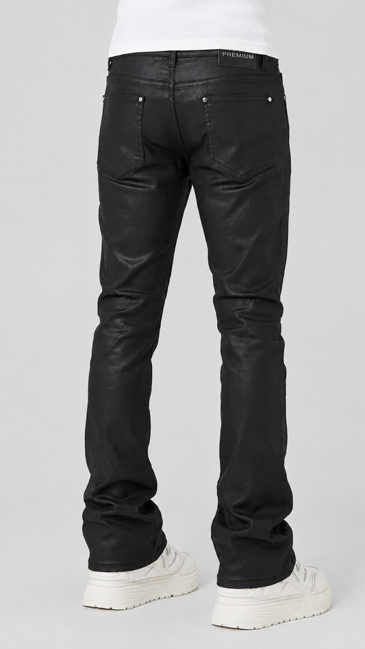 Black leather flare jeans shown from the back on a model wearing a white t-shirt and white platform sneakers, against a light gray studio background.