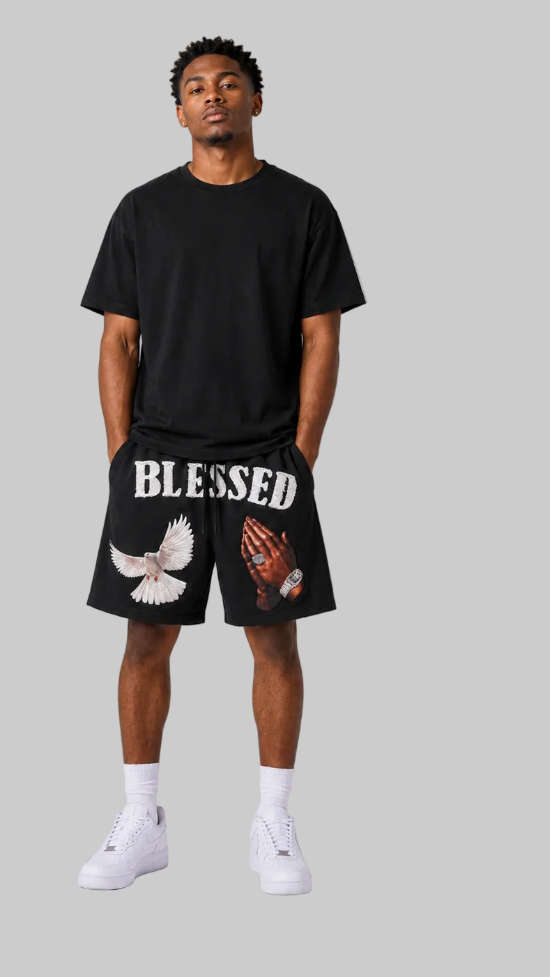 A model shown from the front, wearing a black t-shirt and black shorts. The front view shows a graphic of a praying hand and dove, and the word 'BLESSED' on the shorts.