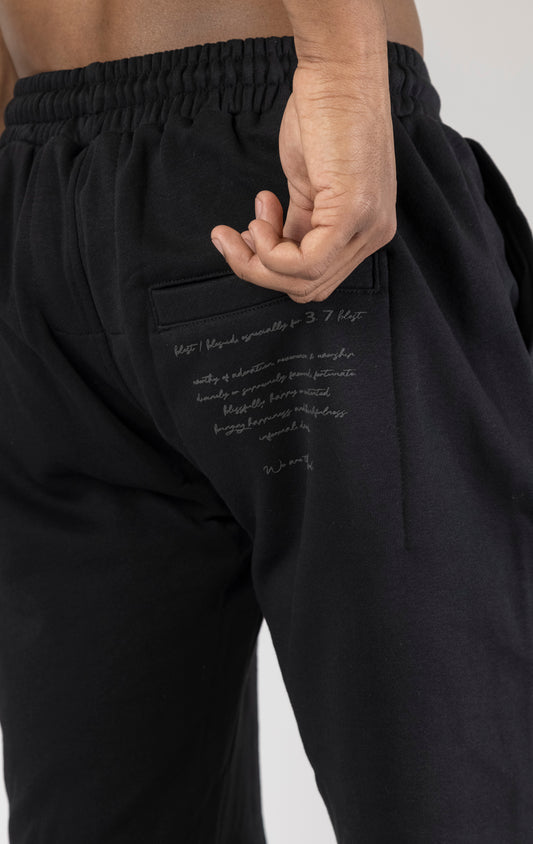 Men's casual, straight-leg shorts in black. The shorts feature a 100% cotton fabric, an arched 3D embroidered "blessed" logo on the front, a tonal raised "blessed" script logo on the back, a back jet pocket, tubular waist drawstrings with metal trims, and a raw hem.