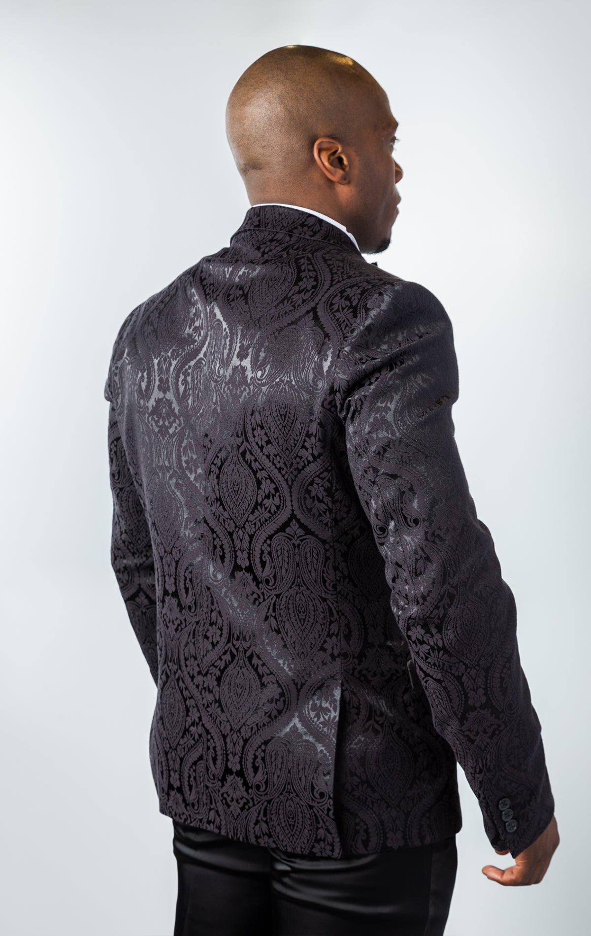 Men's slim-fit blazer in black. The blazer features a paisley patterned poly fabric, peak lapels, one-button closure, and double side vents. 