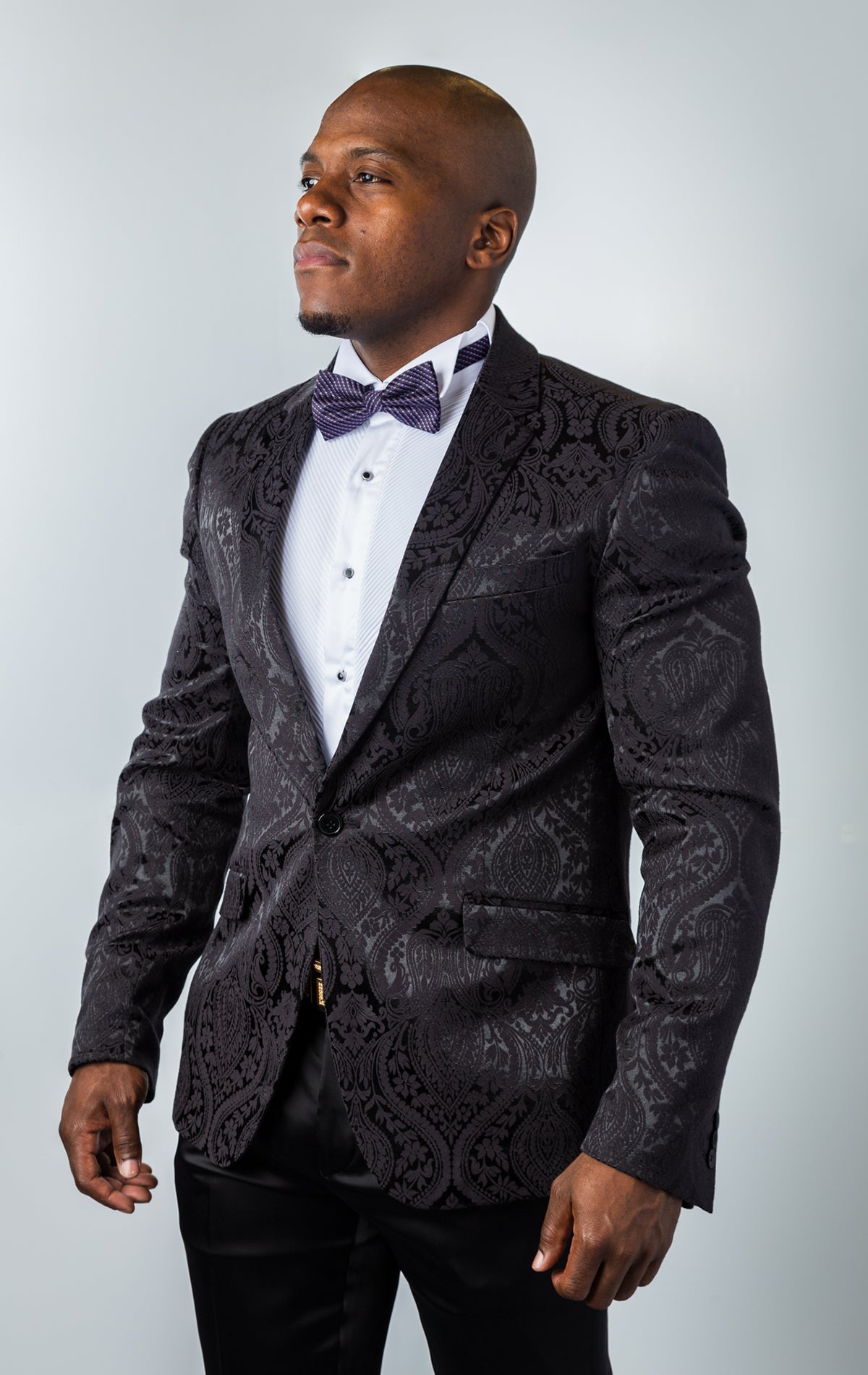 Men's slim-fit blazer in black. The blazer features a paisley patterned poly fabric, peak lapels, one-button closure, and double side vents. 