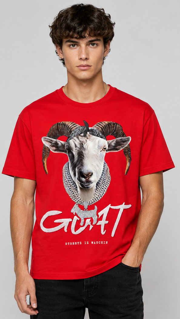 A male model shown from the front  wearing a bright red short-sleeve t-shirt. The front features a large graphic print of a white ram's head with dark horns and the word 'GOAT' in white script below it.