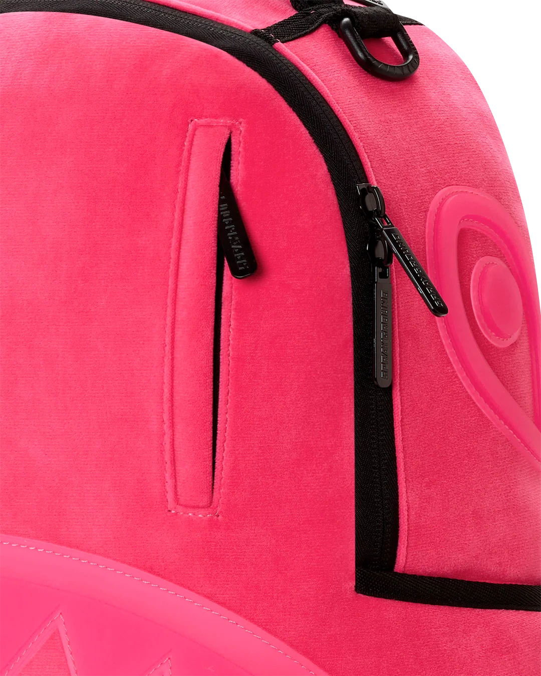 Close-up of a bright pink backpack with black zipper trim and a vertical zip pocket, showing the brand name 'sprayground' on the zipper pull.