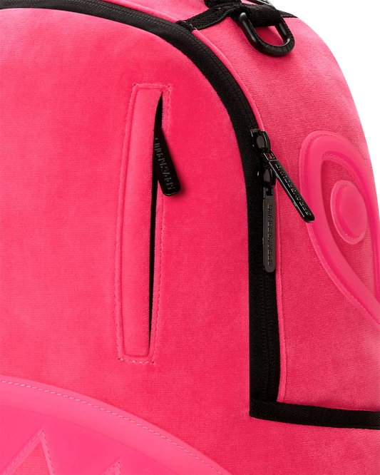 Close-up of a bright pink backpack with black zipper trim and a vertical zip pocket, showing the brand name 'sprayground' on the zipper pull.