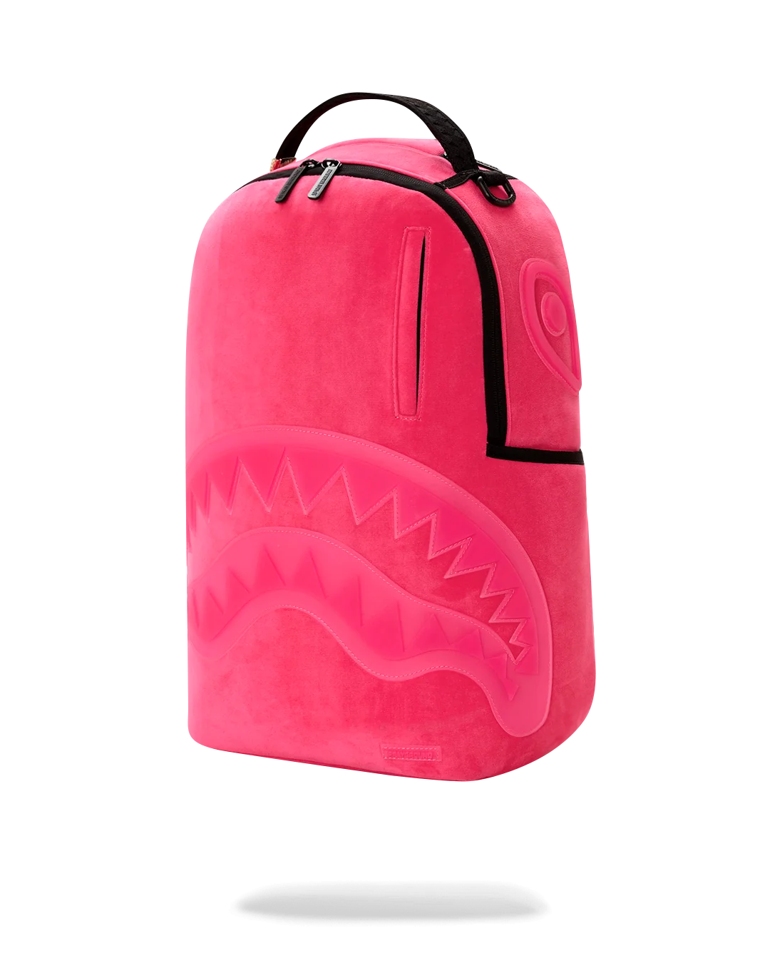 A bright pink plush backpack with a shark-face design on the front, black trim, and a top carry handle, shown on a clean white background.