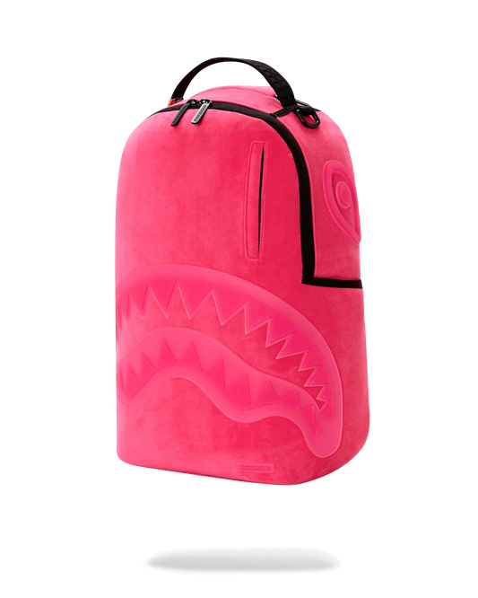 A bright pink plush backpack with a shark-face design on the front, black trim, and a top carry handle, shown on a clean white background.