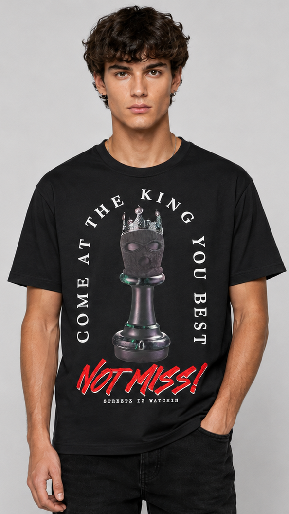 A black short-sleeve graphic T-shirt shown on a male model from the front against a light gray studio background. The front features a large chess-themed graphic with a chess piece, white curved text reading 'COME AT THE KING YOU BEST', and red text reading 'NOT MISS!'.
