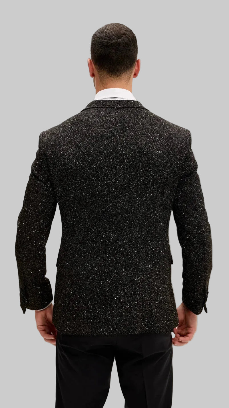 A man viewed from the back wearing a dark blazer over a white collared shirt and black trousers, set against a plain off-white background.