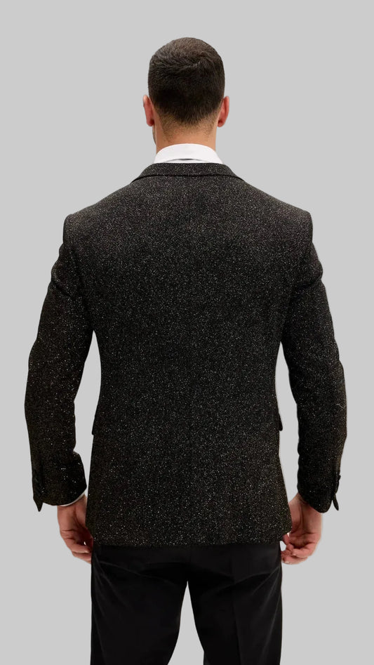 A man viewed from the back wearing a dark blazer over a white collared shirt and black trousers, set against a plain off-white background.