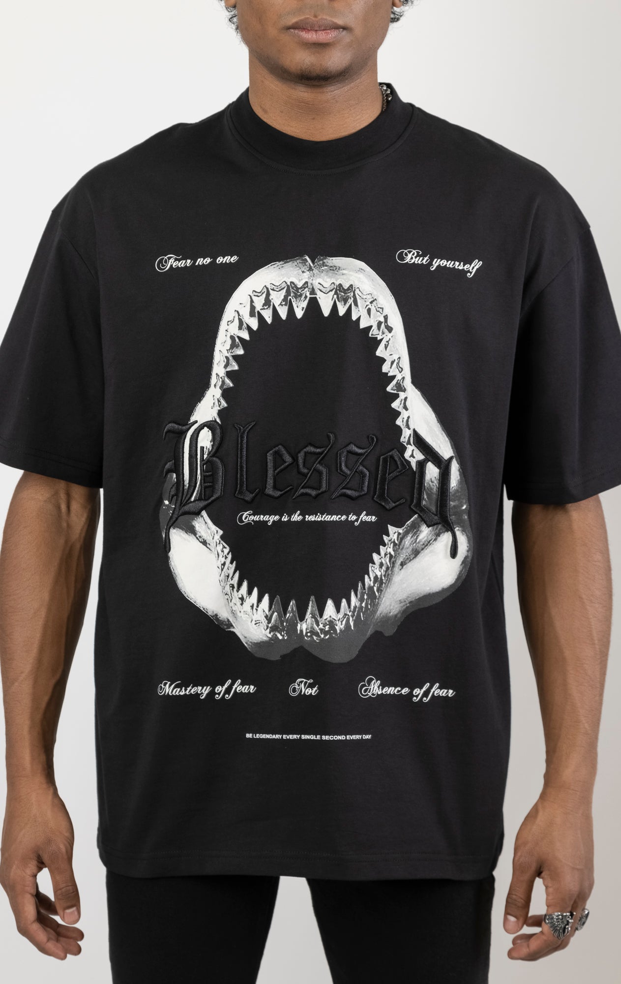 Men's boxy fit t-shirt in black. The shirt features dropped shoulders, longer sleeves, and a wide, fitted neck rib. It has a "Courage" front print with 3D embroidery. Made from 100% cotton jersey (190gsm). A "blessed" slogan is printed on the inner neck binding.