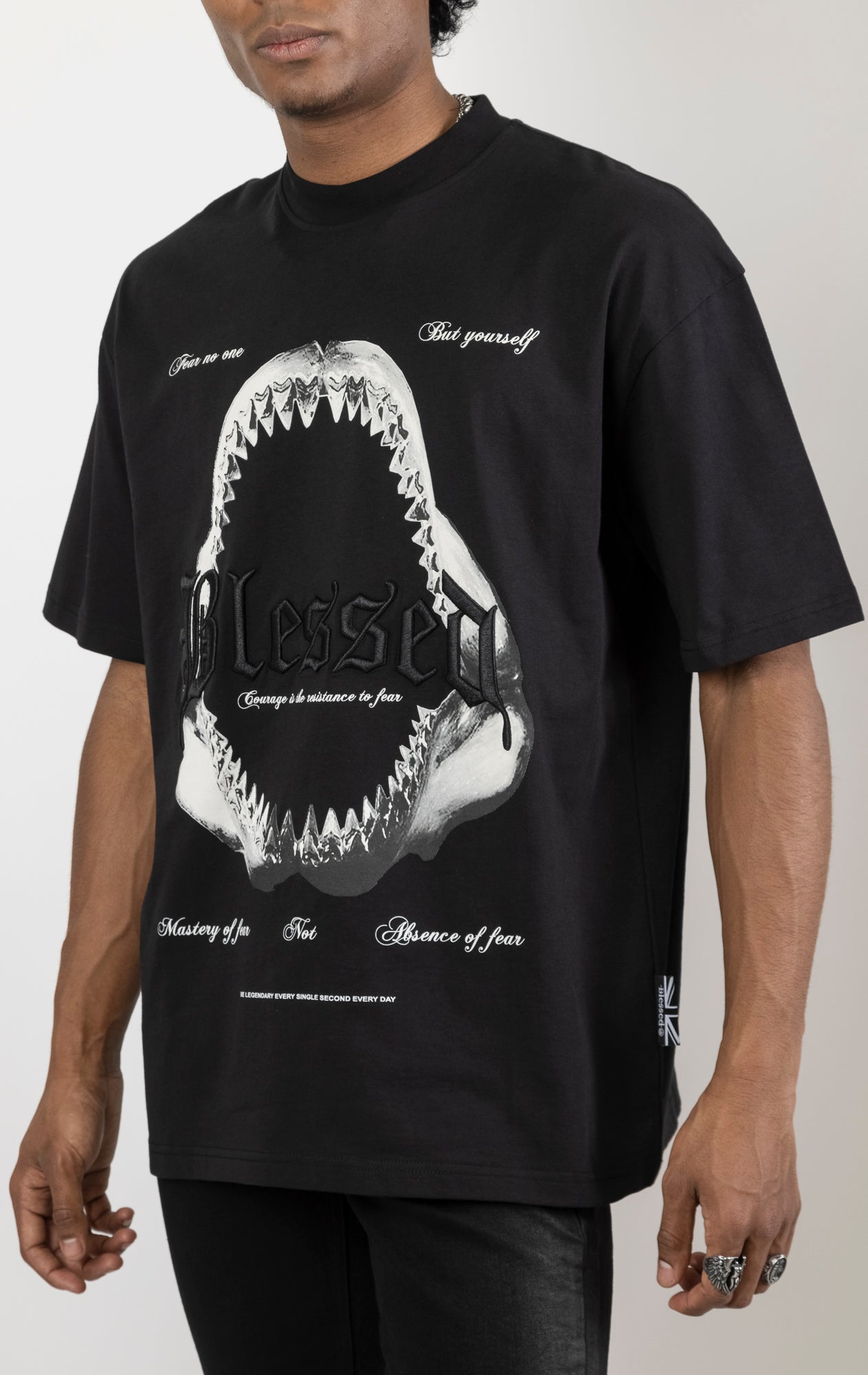 Men's boxy fit t-shirt in black. The shirt features dropped shoulders, longer sleeves, and a wide, fitted neck rib. It has a "Courage" front print with 3D embroidery.  Made from 100% cotton jersey (190gsm).  A "blessed" slogan is printed on the inner neck binding.