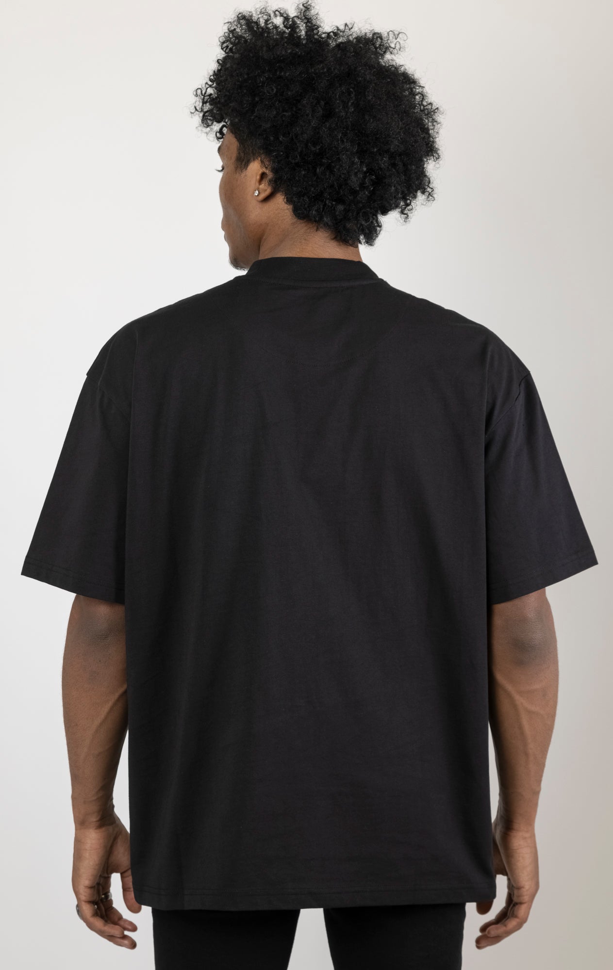 Men's boxy fit t-shirt in black. The shirt features dropped shoulders, longer sleeves, and a wide, fitted neck rib. It has a "Courage" front print with 3D embroidery. Made from 100% cotton jersey (190gsm). A "blessed" slogan is printed on the inner neck binding.