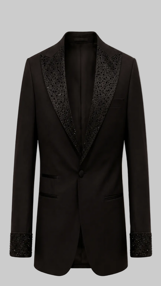 A black single-breasted tuxedo jacket with ornate black beaded lapels and matching beaded cuff trim, shown against a solid pale pink background.