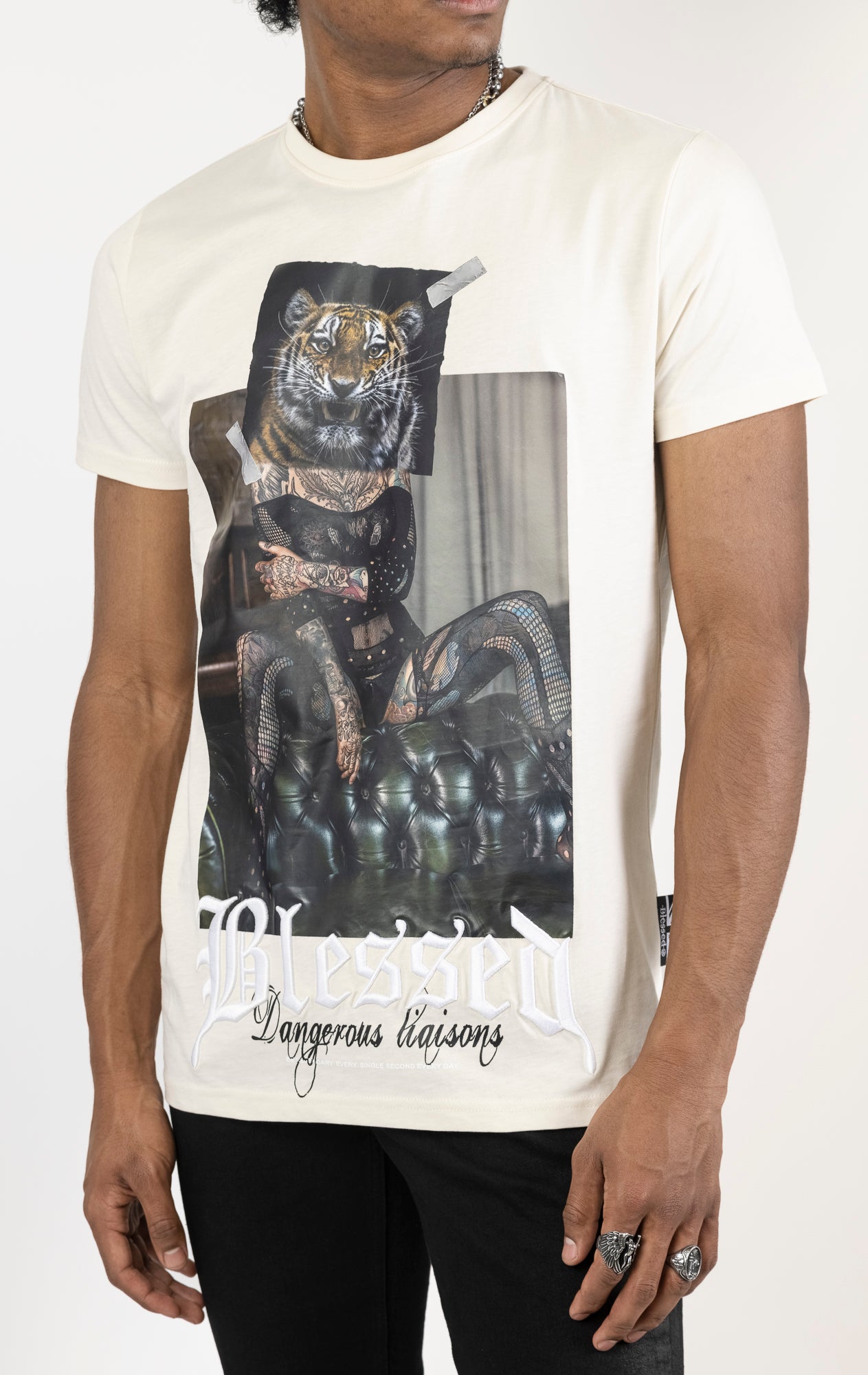 Men's regular fit t-shirt in eggshell color. The shirt features a slightly elongated sleeve, a fitted neckline, and a straight body. It has a "Dangerous Liaisons" front print with 3D embroidery. Made from 100% cotton jersey (190gsm). A "blessed" slogan is printed on the inner neck binding and a woven side seam tab with "blessed" is also included.