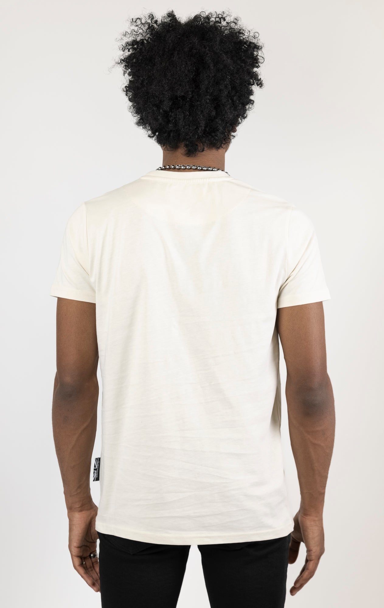 Men's regular fit t-shirt in eggshell color. The shirt features a slightly elongated sleeve, a fitted neckline, and a straight body. It has a "Dangerous Liaisons" front print with 3D embroidery. Made from 100% cotton jersey (190gsm). A "blessed" slogan is printed on the inner neck binding and a woven side seam tab with "blessed" is also included.